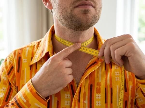 Man meet de boordmaat van zijn retro overhemd met een meetlint rond zijn nek