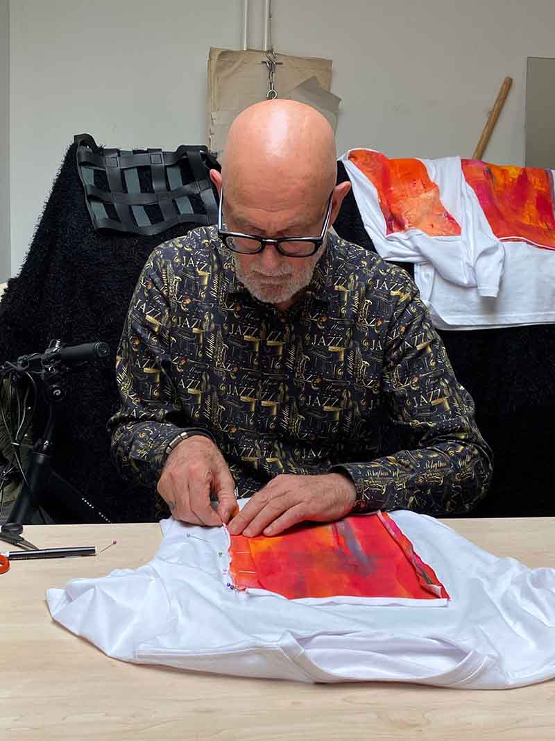 Ontwerper Vincent Welten werkt in zijn atelier aan een exclusief No106 design T-shirt. Hij speldt met de hand een kleurrijk, abstract kunstwerk in oranje en rode tinten op een wit T-shirt.